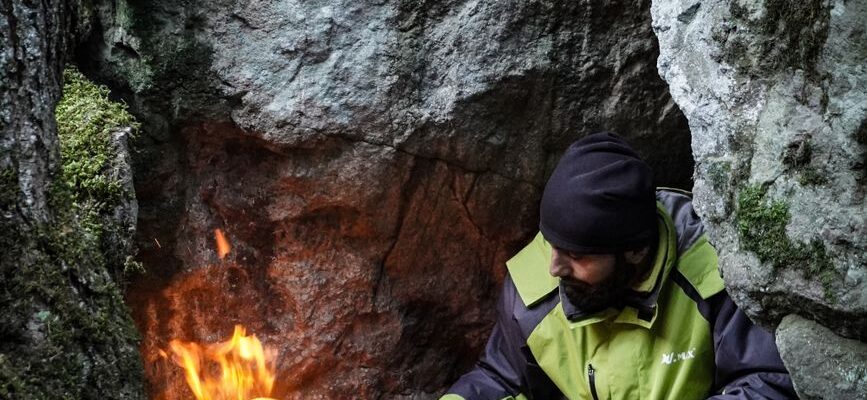 survivalist lighting campfire in mountain cave